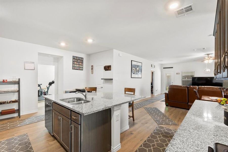 Kitchen featuring dark brown cabinetry, light stone counters, open floor plan, light wood-style flooring, and a kitchen breakfast bar