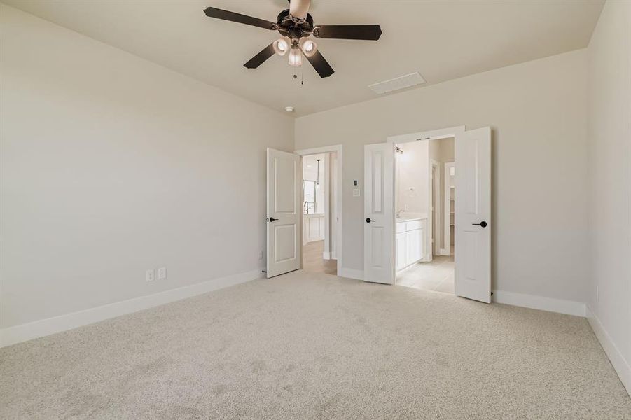 Unfurnished bedroom featuring light carpet, ensuite bath, and a ceiling fan