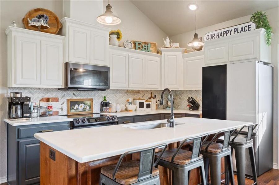 Kitchen featuring stainless steel appliances, a kitchen breakfast bar, decorative backsplash, pendant lighting, and an island with sink
