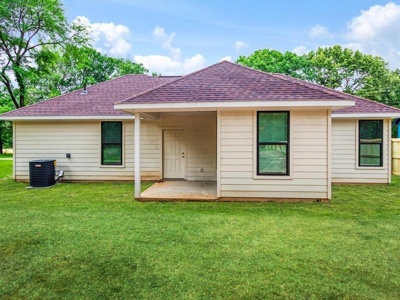 Rear exterior with a covered patio, beige siding, black-framed windows, and a shingle roof Rear exterior with a covered patio, beige siding, black-framed windows, and a shingle roof