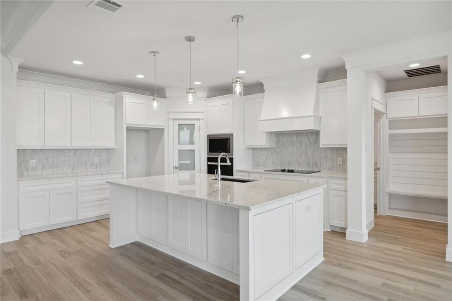 Kitchen with light hardwood / wood-style flooring, premium range hood, and tasteful backsplash