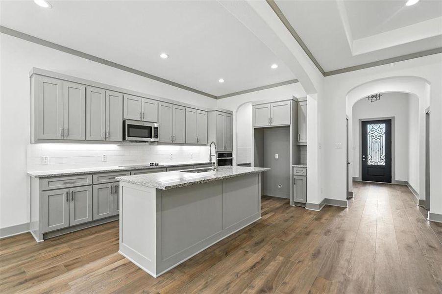 Kitchen featuring backsplash, recessed lighting, dark wood finished floors, light stone countertops, and an island with sink Kitchen featuring backsplash, recessed lighting, dark wood finished floors, light stone countertops, and an island with sink