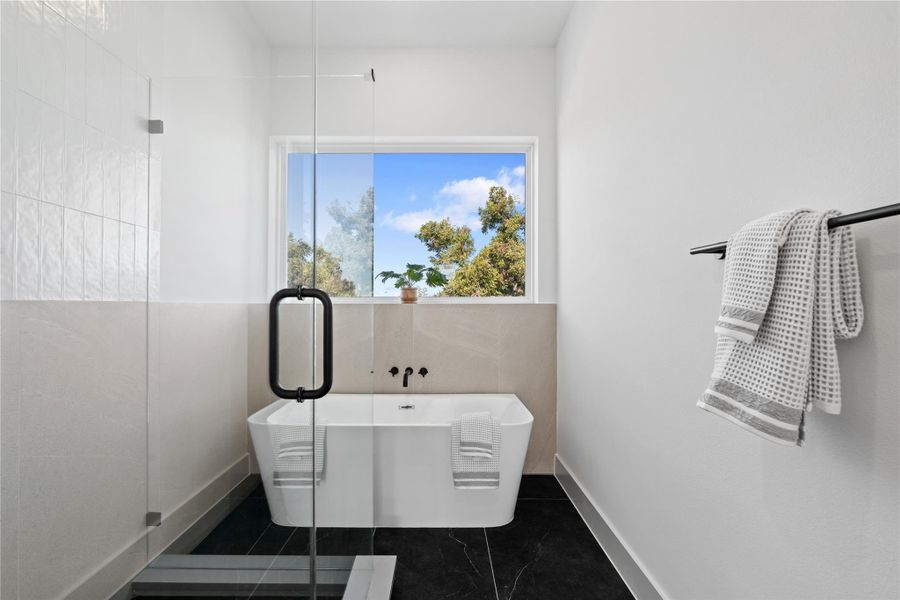 A frameless glass shower with linear drains sits beside a sculptural soaking tub, all framed by a picture window that washes the space in natural light. A frameless glass shower with linear drains sits beside a sculptural soaking tub, all framed by a picture window that washes the space in natural light.