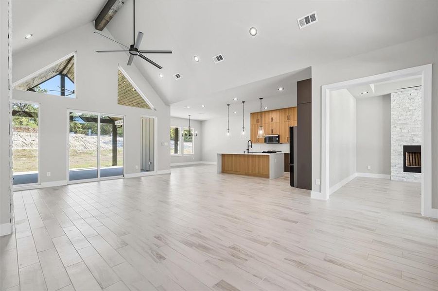 Unfurnished living room featuring high vaulted ceiling, beam ceiling, light wood-style floors, a fireplace, and ceiling fan Unfurnished living room featuring high vaulted ceiling, beam ceiling, light wood-style floors, a fireplace, and ceiling fan