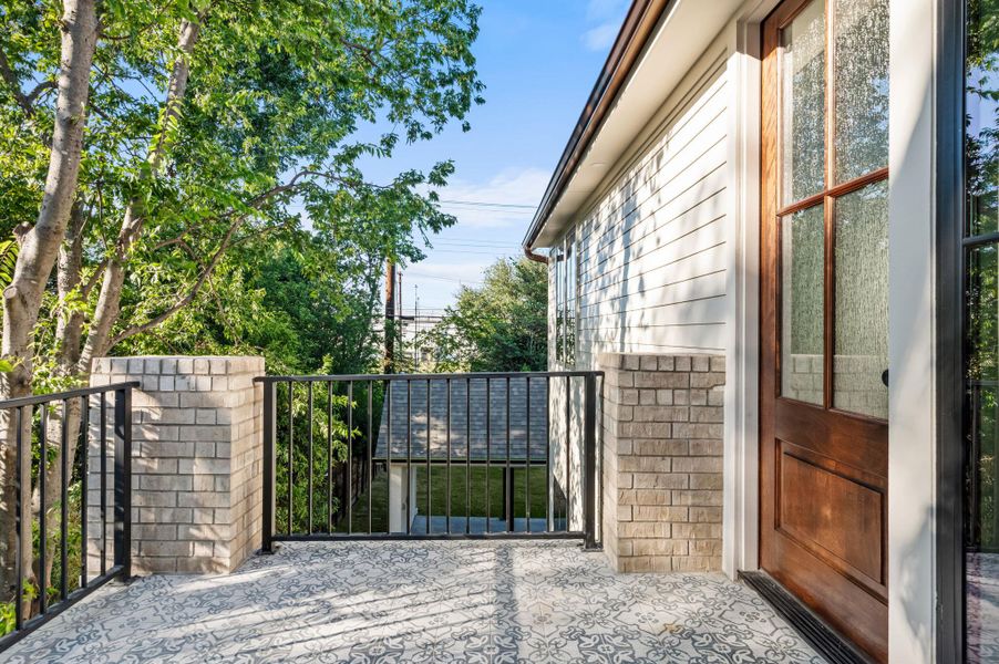 An inviting exterior balcony with decorative tile flooring and wrought iron railings offers treetop views.