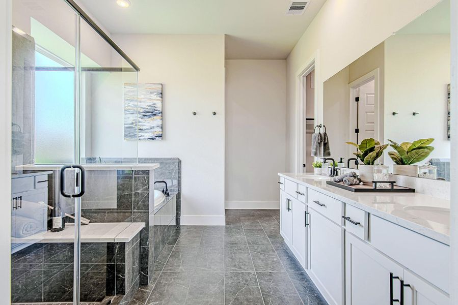 Unwind in this luxurious bathroom featuring a glass-enclosed shower with built-in bench, a soaking tub, and dual vanities with quartz countertops.