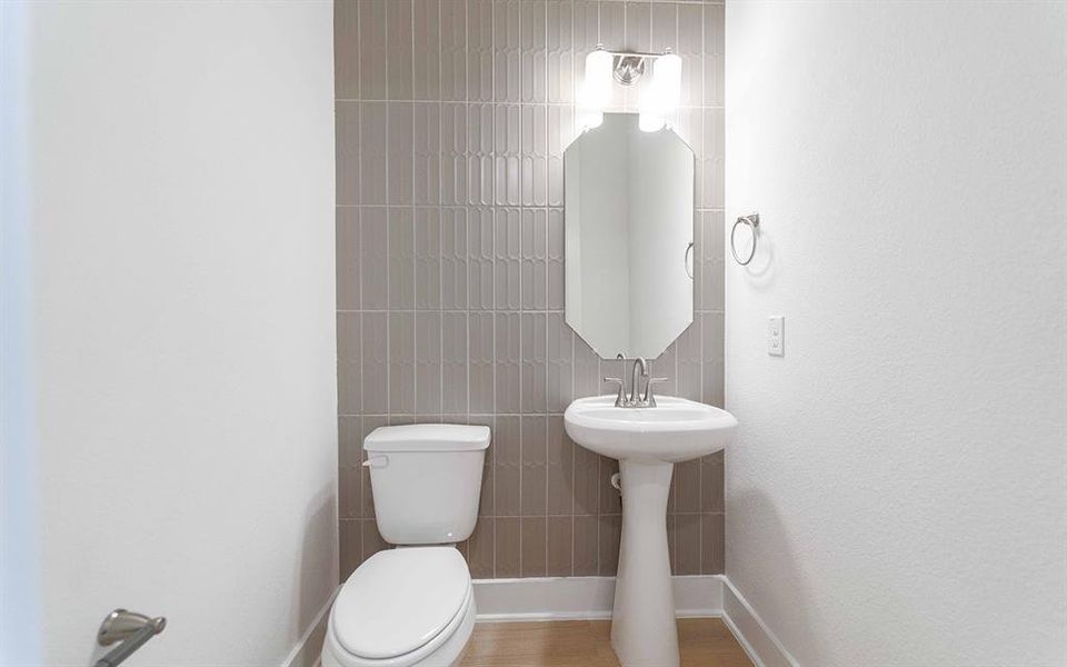 Bathroom featuring a pedestal sink, wall-mounted mirror, and stylish vertical tile accent wall