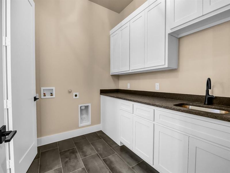 Laundry area featuring sink, washer hookup, cabinets, hookup for an electric dryer, and dark tile patterned floors