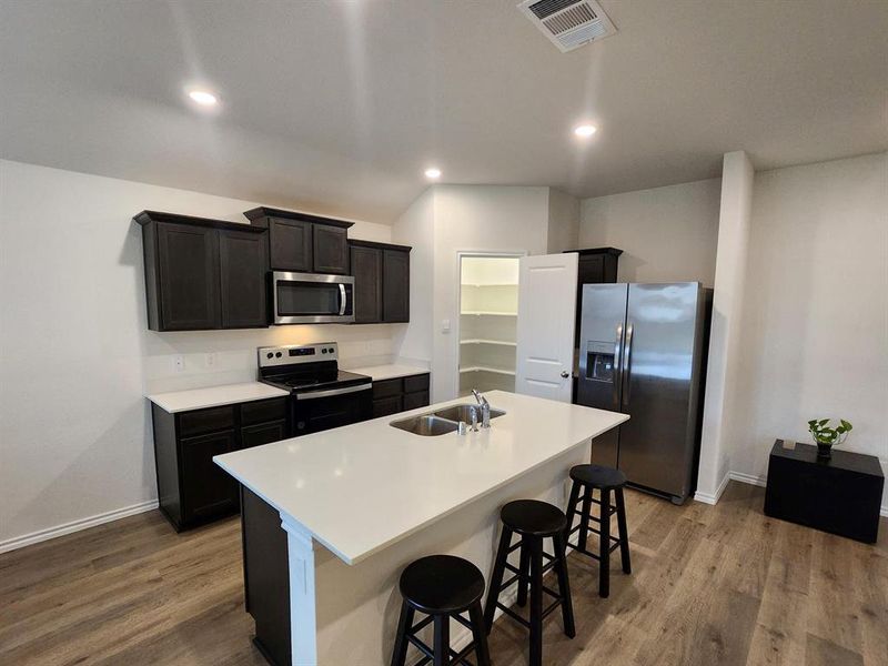 Kitchen with range, stainless steel refrigerator, a kitchen bar, an island with sink, and dark wood-style flooring