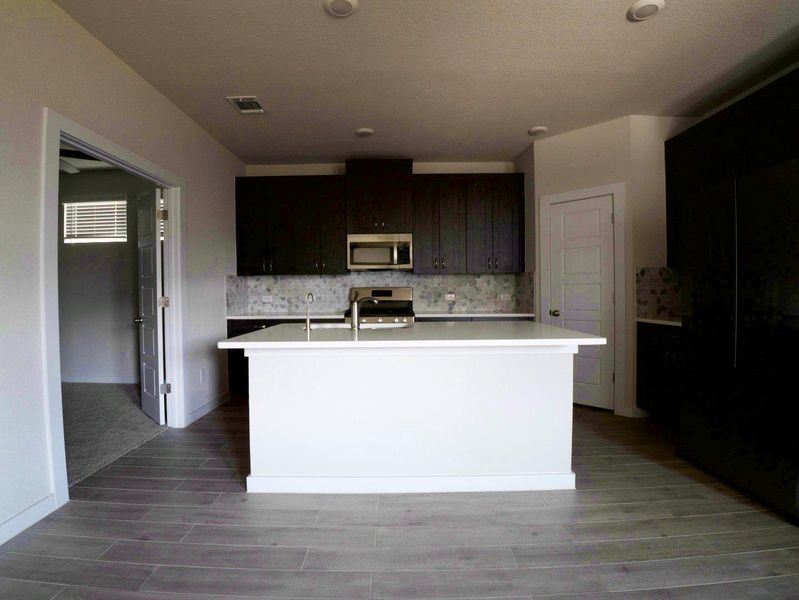 Kitchen featuring a center island with sink, decorative backsplash, appliances with stainless steel finishes, and wood finish floors Kitchen featuring a center island with sink, decorative backsplash, appliances with stainless steel finishes, and wood finish floors