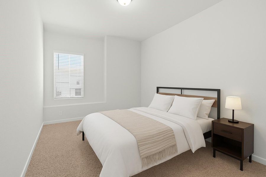 Cozy bedroom with neutral tones, featuring a comfortable bed, bedside table with lamp, and a window with blinds for natural light.