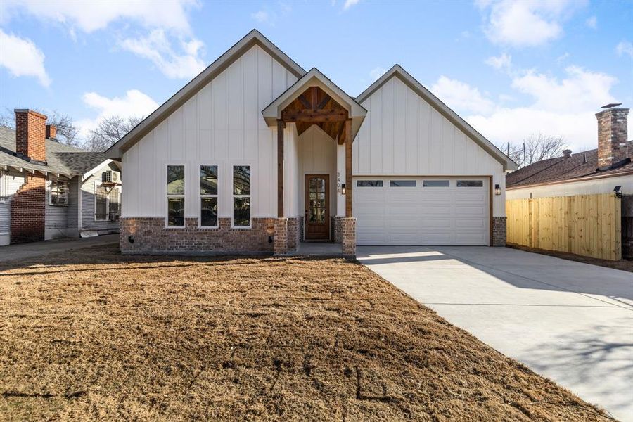 Modern farmhouse with an attached garage, brick siding, fence, driveway, and board and batten siding