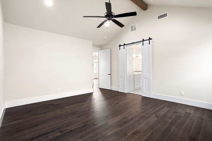 Unfurnished bedroom with dark wood-type flooring, connected bathroom, ceiling fan, and a barn door