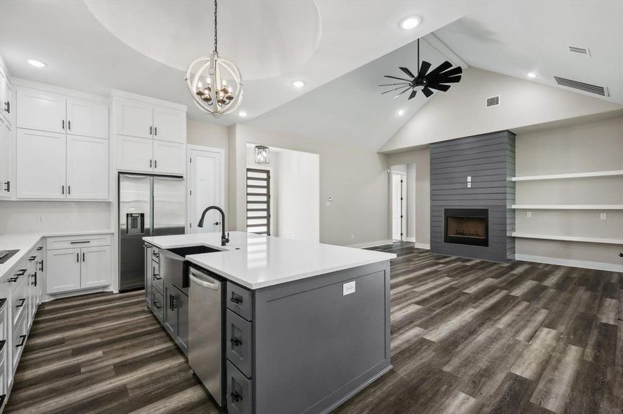 Kitchen featuring a kitchen island with sink, white cabinetry, stainless steel appliances, and a fireplace