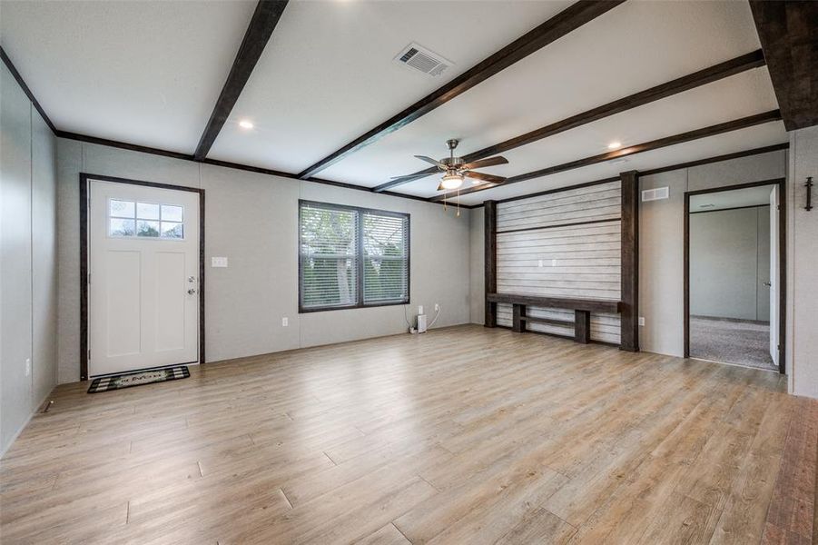Unfurnished living room with ceiling fan, light wood-style floors, and beamed ceiling Unfurnished living room with ceiling fan, light wood-style floors, and beamed ceiling