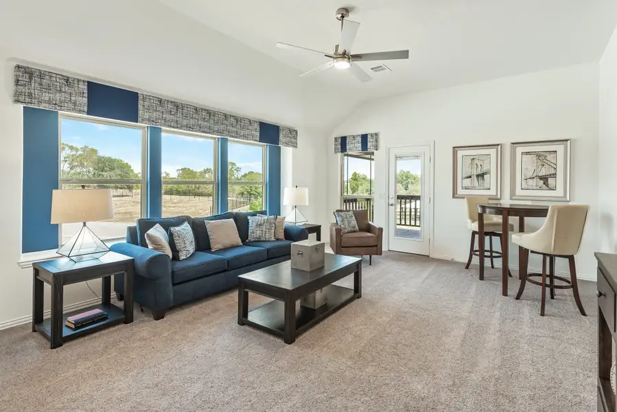 Living room with blue sofa, vaulted ceiling, ceiling fan, and large windows with outdoor views
