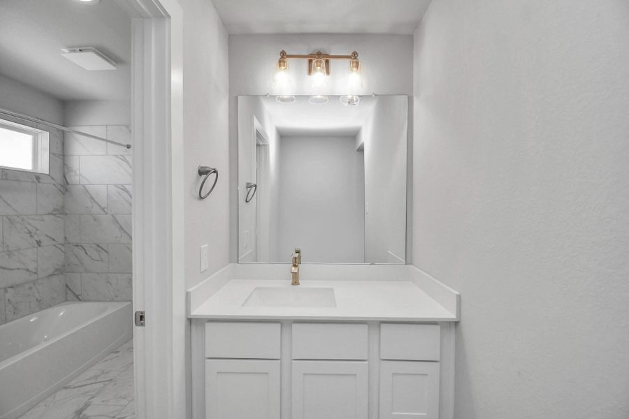 Secondary bath features tile flooring, bath/shower combo with tile surround, light stained wood cabinets, beautiful light countertop.