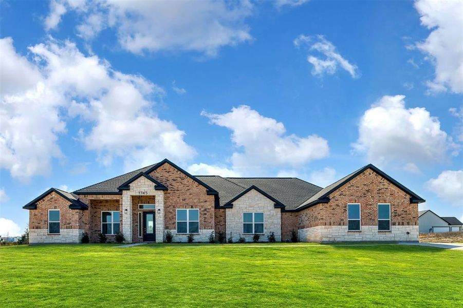 View of front facade with a shingled roof, a front yard, and brick siding