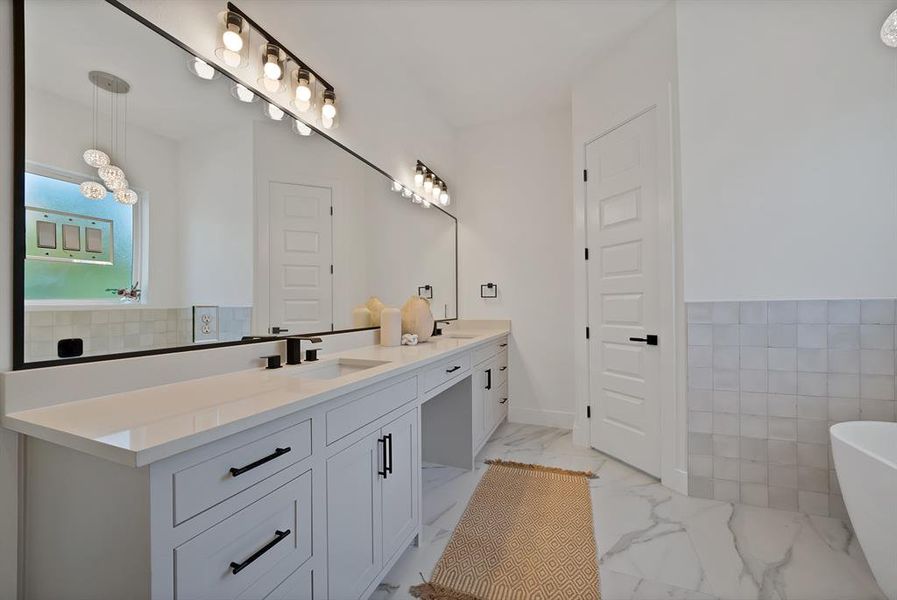 Full bathroom with double vanity, a freestanding bath, tile walls, and light marble finish flooring Full bathroom with double vanity, a freestanding bath, tile walls, and light marble finish flooring