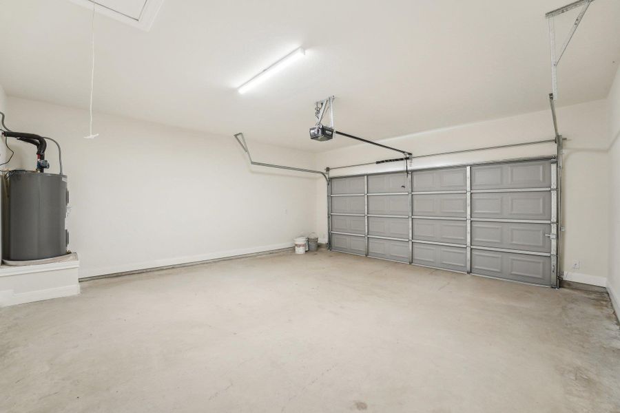 Garage with baseboards, a garage door opener, and electric water heater Garage with baseboards, a garage door opener, and electric water heater