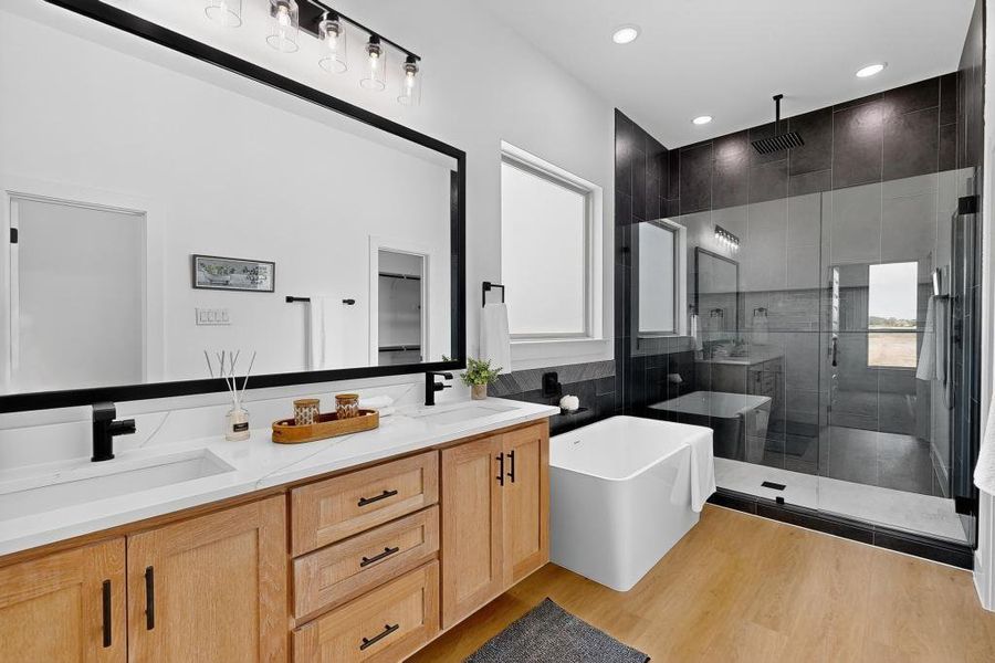Bathroom featuring a shower stall, double vanity, a freestanding tub, wood finished floors, and recessed lighting