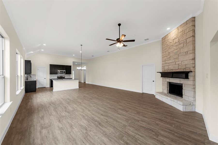 Open concept living area featuring a stone fireplace with a dark wood mantel, high vaulted ceilings, and wood-finish flooring
