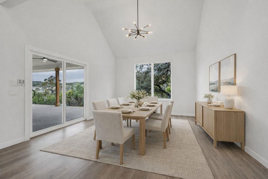 Dining space with high vaulted ceiling, healthy amount of natural light, light wood finished floors, and a chandelier