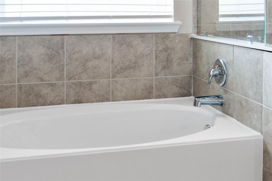 Indulge in the primary bath's deep, built-in soaking tub with elegant chrome fixtures and a sleek tile surround for a true spa-like retreat.
