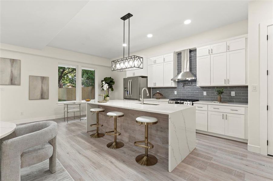 Kitchen with wall chimney exhaust hood, stainless steel fridge with ice dispenser, light wood-style flooring, a breakfast bar area, and recessed lighting Kitchen with wall chimney exhaust hood, stainless steel fridge with ice dispenser, light wood-style flooring, a breakfast bar area, and recessed lighting