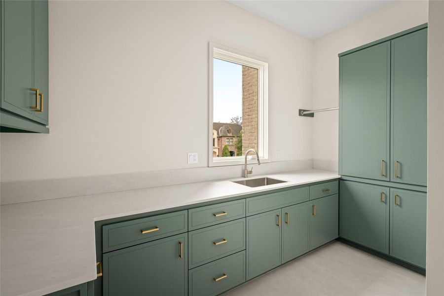 A functional laundry space with abundant cabinetry, expansive work surfaces, and a window-side utility sink.