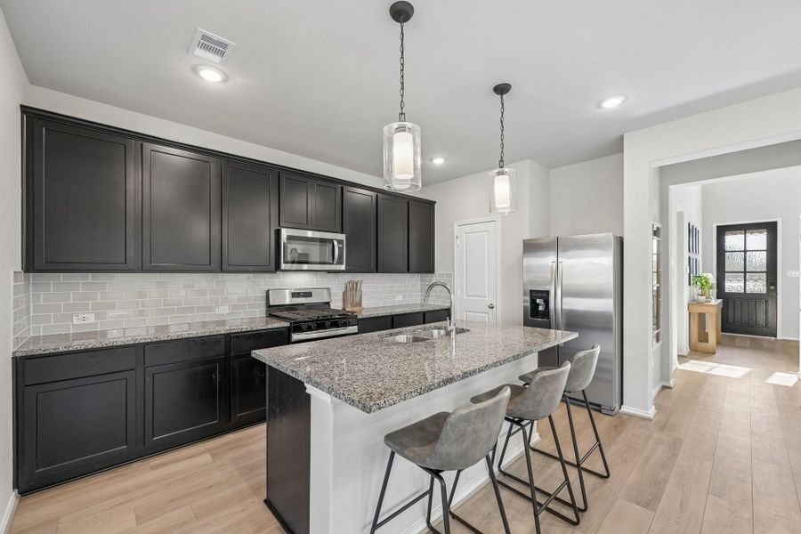 Sleek modern kitchen with dark cabinetry, granite countertops, and stainless steel appliances. Features a spacious island with seating for three and elegant pendant lighting.