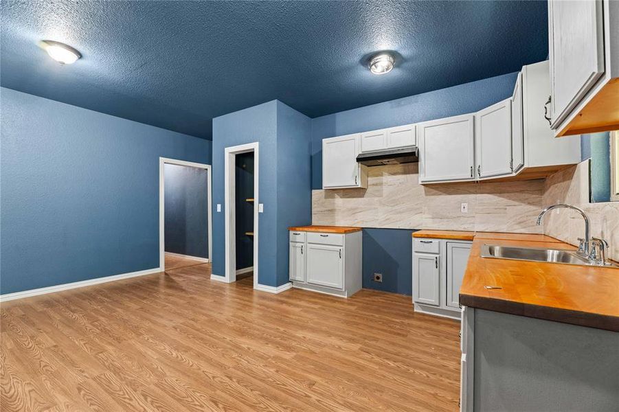 Kitchen featuring light hardwood / wood-style flooring, tasteful backsplash, white cabinetry, wooden counters, and sink Kitchen featuring light hardwood / wood-style flooring, tasteful backsplash, white cabinetry, wooden counters, and sink
