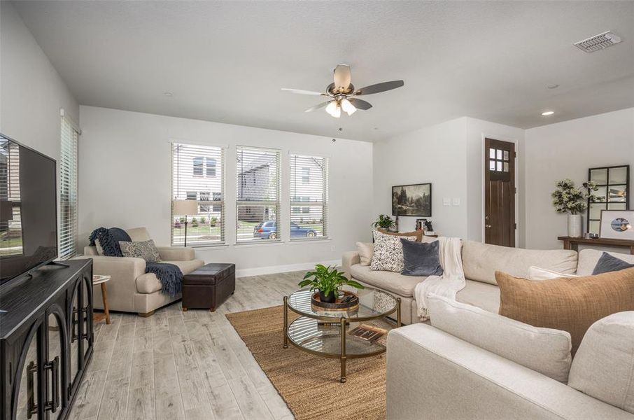 Spacious living room with wide-plank wood-look tile flooring, ceiling fan, and a wall of windows bringing in natural light.