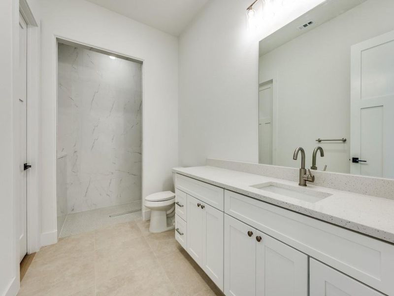 Bathroom featuring toilet, vanity, tile patterned flooring, and tiled shower