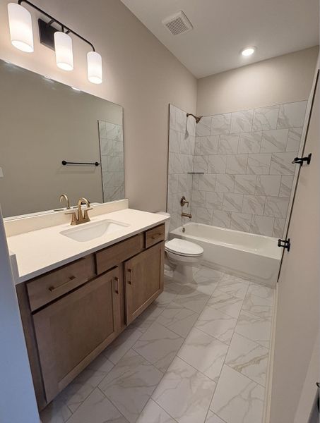 Bathroom featuring a single vanity with light wood cabinetry, a light-colored countertop, and a rectangular undermount sink with a bronze-finish faucet