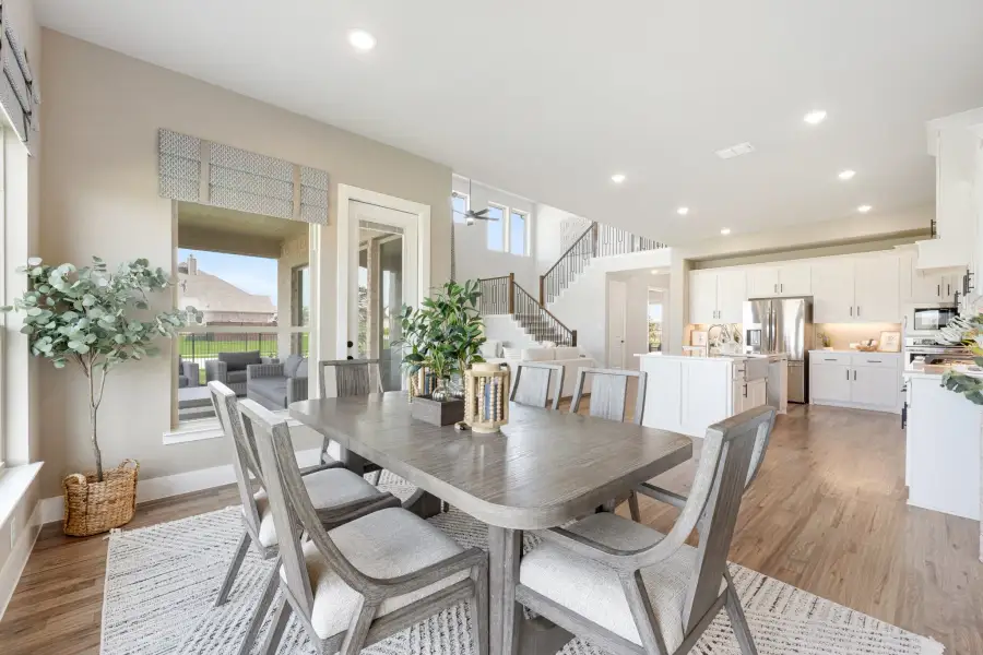 Open-concept dining area with gray wood table, six chairs, and view of white kitchen and staircase beyond. Open-concept dining area with gray wood table, six chairs, and view of white kitchen and staircase beyond.