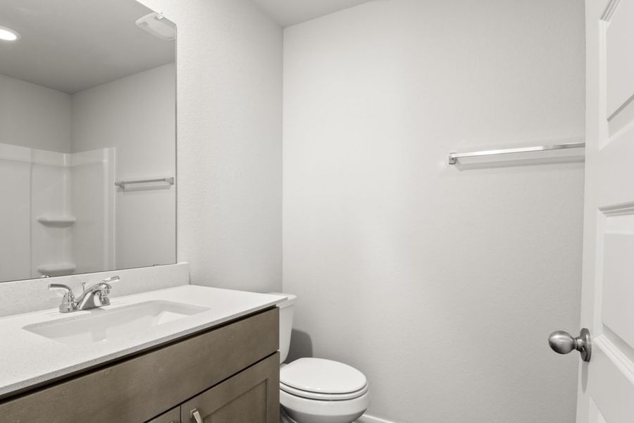 Image of a bathroom with light grey walls, a white vanity with brown cabinets and a mirror Image of a bathroom with light grey walls, a white vanity with brown cabinets and a mirror