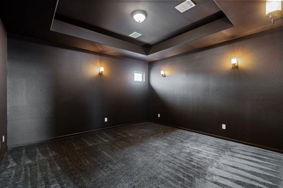A modern media room outfitted with dark walls and ceiling, complemented by soft wall lighting creating an ideal ambiance for entertainment.