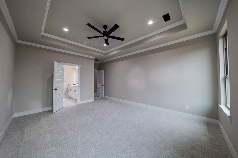 Unfurnished bedroom featuring crown molding, ceiling fan, ensuite bathroom, light carpet, and a raised ceiling