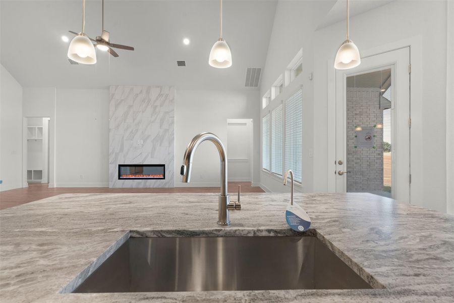 Kitchen with open floor plan, a premium fireplace, a ceiling fan, light stone counters, and pendant lighting