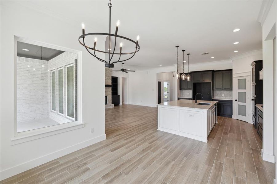 Kitchen featuring ceiling fan with notable chandelier, light hardwood / wood-style flooring, decorative light fixtures, sink, and a center island with sink