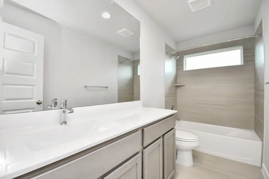 Secondary bath features tile flooring, bath/shower combo with tile surround, light stained wood cabinets, beautiful light countertop.