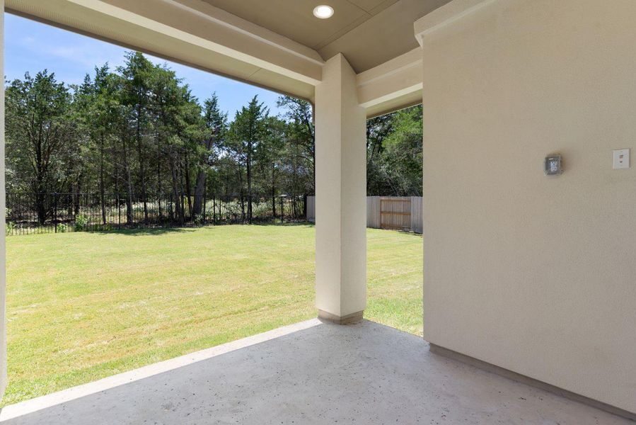 A spacious covered patio overlooks a generous green lawn and a natural treeline beyond.