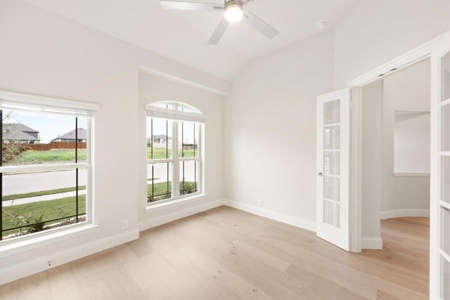 Empty room with light wood floors, arched window, ceiling fan, and French doors