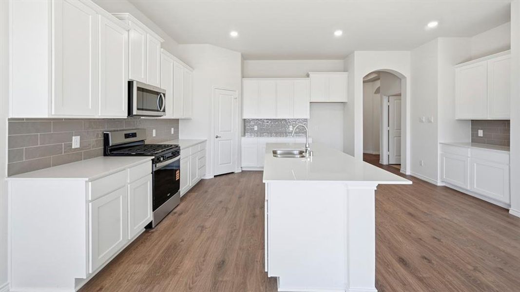 Kitchen with appliances with stainless steel finishes, backsplash, arched walkways, white cabinetry, and a center island with sink