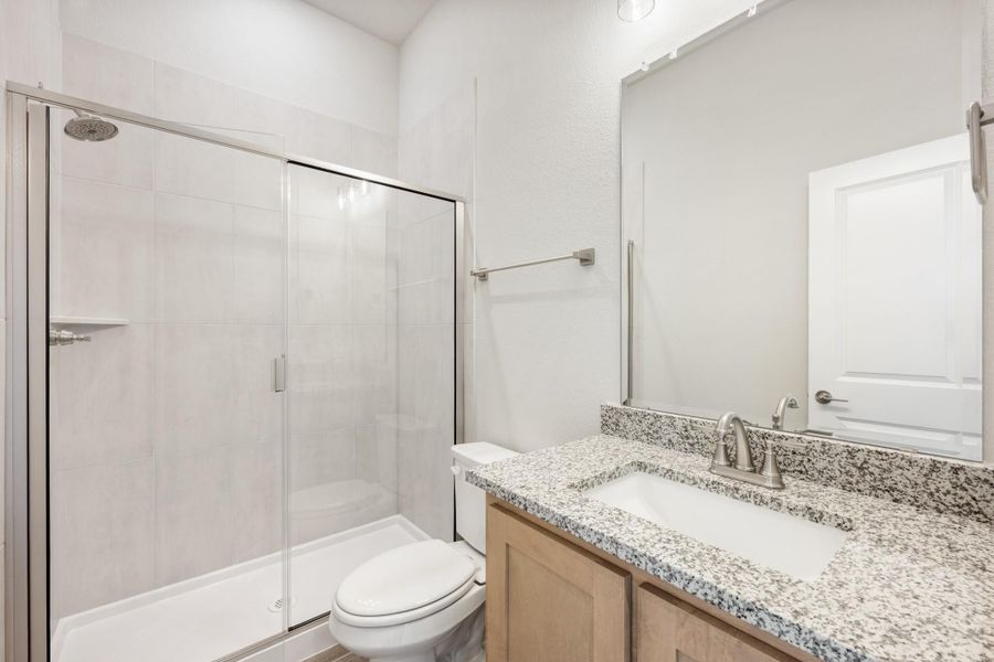 Bathroom with glass-door walk-in shower, granite vanity countertop, and wood cabinets