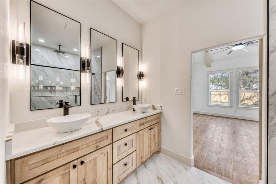 Full bathroom featuring double vanity, light marble finish floors, and a marble finish shower