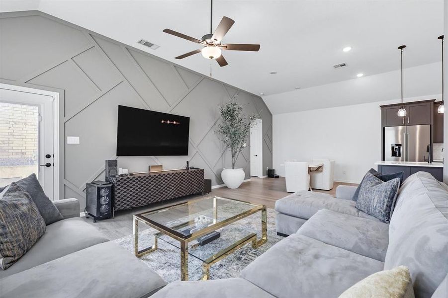 Living room with lofted ceiling, wood finished floors, ceiling fan, and an accent wall
