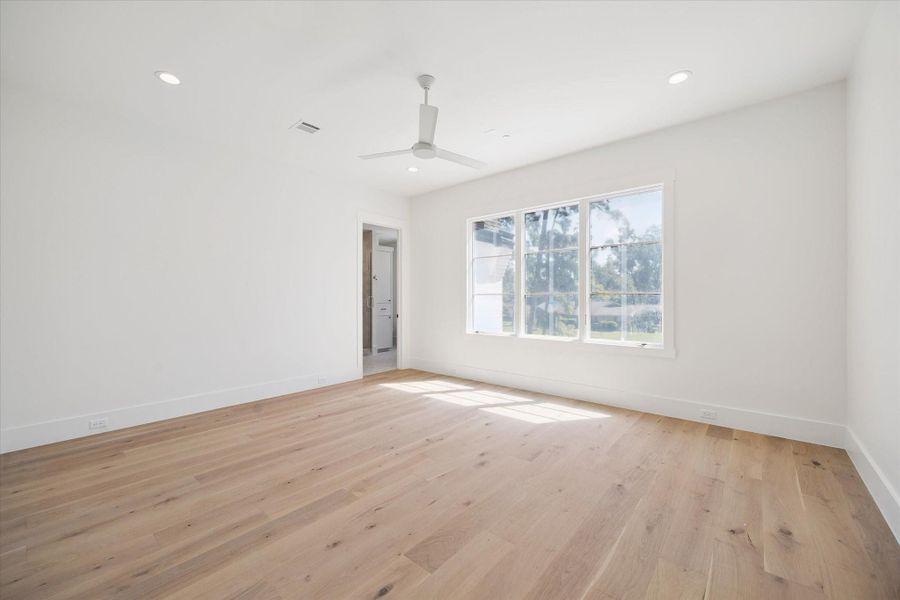 This bright, spacious room features natural wood flooring, a large window for ample sunlight, recessed lighting, and a ceiling fan. An adjacent doorway leads to an en-suite bathroom, adding convenience and privacy. This bright, spacious room features natural wood flooring, a large window for ample sunlight, recessed lighting, and a ceiling fan. An adjacent doorway leads to an en-suite bathroom, adding convenience and privacy.