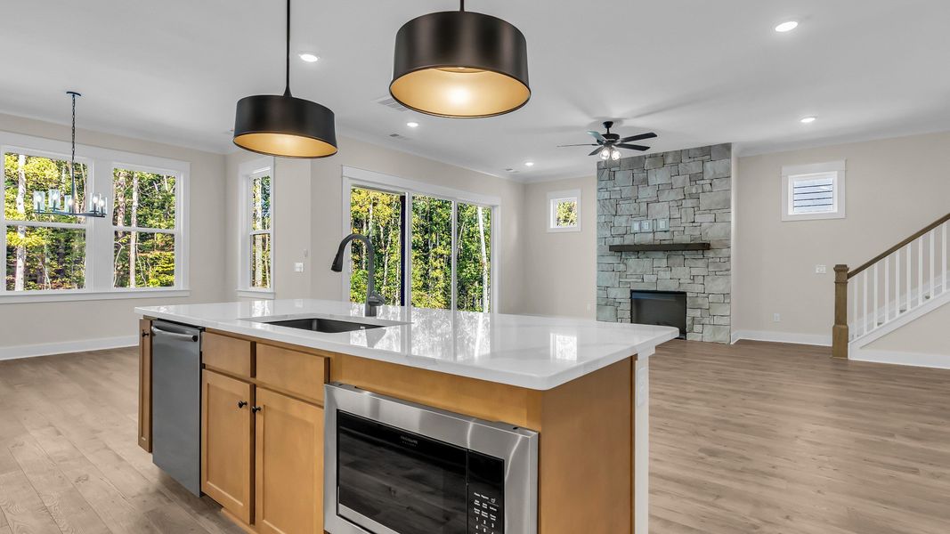Kitchen with wood colored cabinetry and nearby gathering room (Representative of completed home)